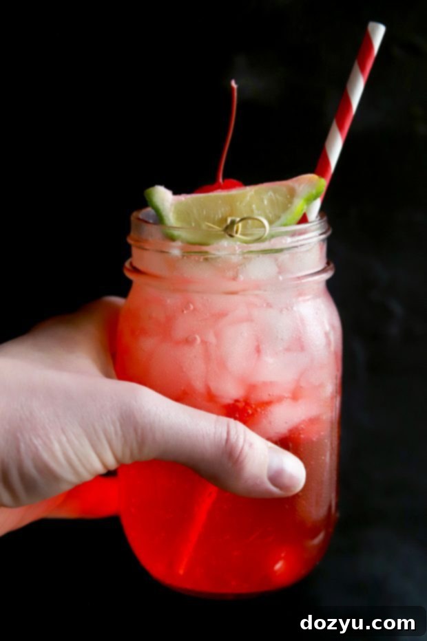 A refreshing bubbly cherry and lime cocktail held in a mason jar, garnished with fresh fruit, ideal for summer.