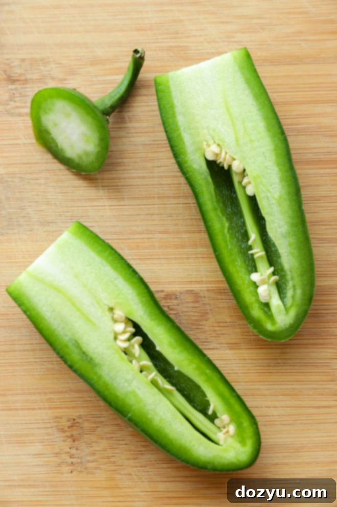 A jalapeño pepper sliced in half lengthwise on a cutting board, revealing the seeds and white membrane inside.