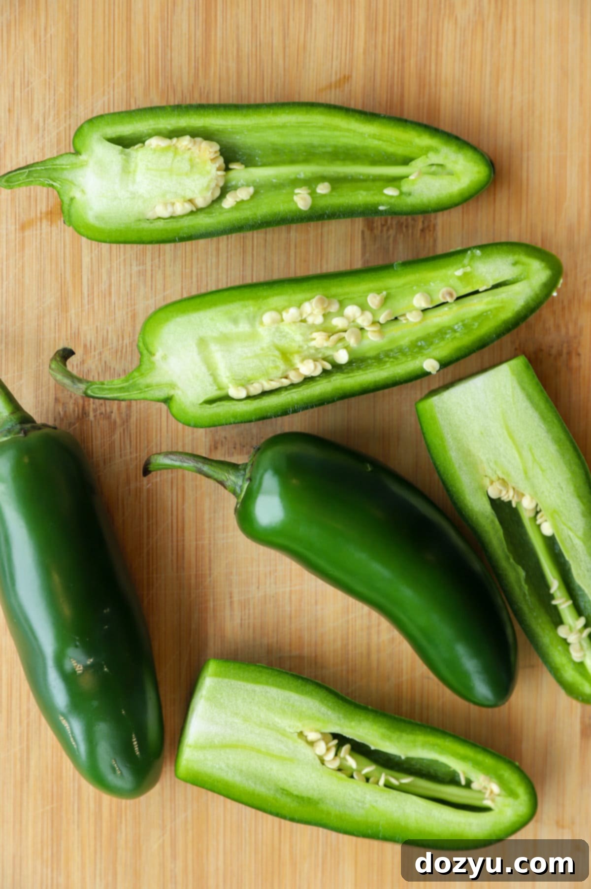Overhead image of jalapeño peppers on a cutting board, illustrating the process of how to seed a jalapeño.