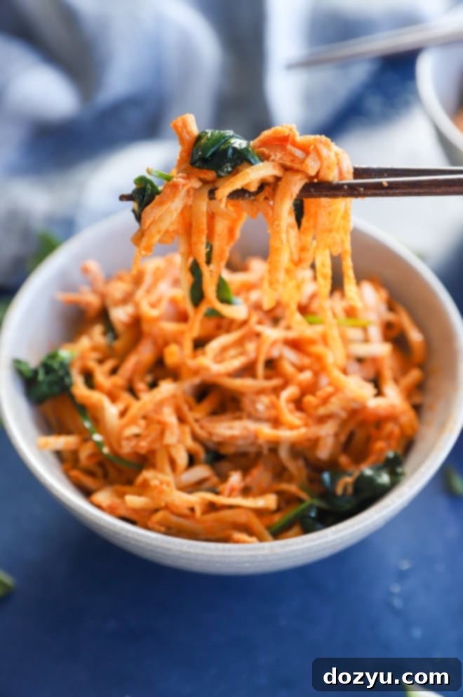 Chopsticks holding Korean Gochujang noodles with chicken and spinach from a bowl