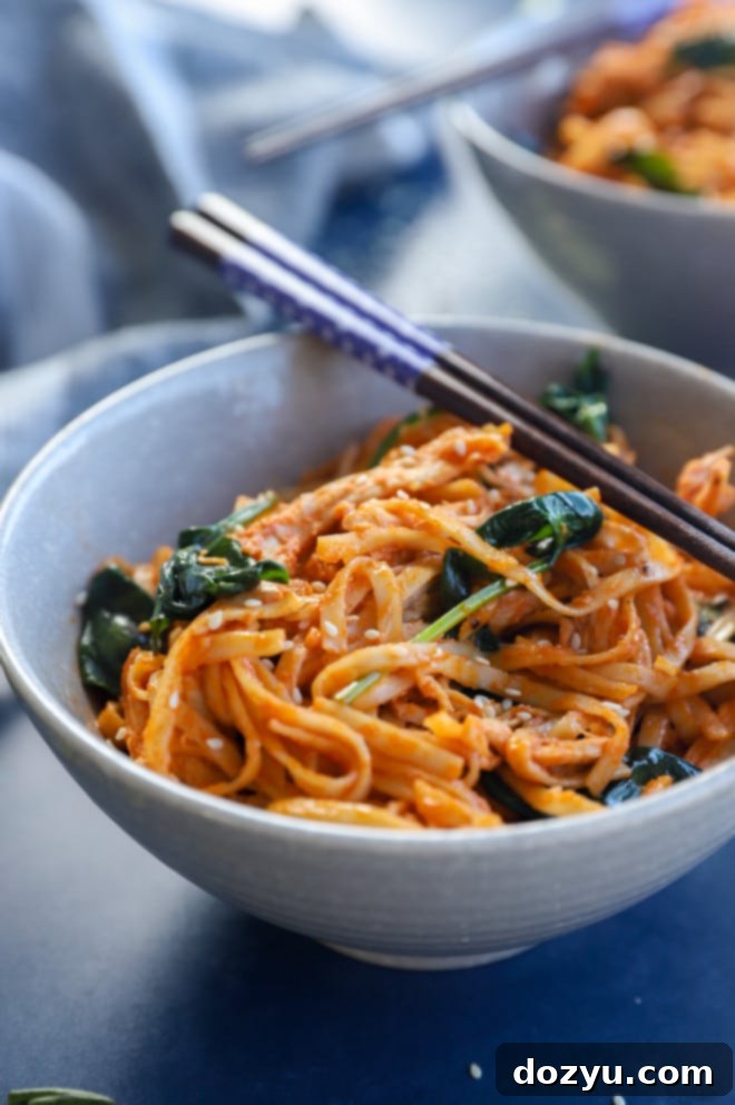 Gochujang noodles with chicken and spinach in a bowl, being held by chopsticks
