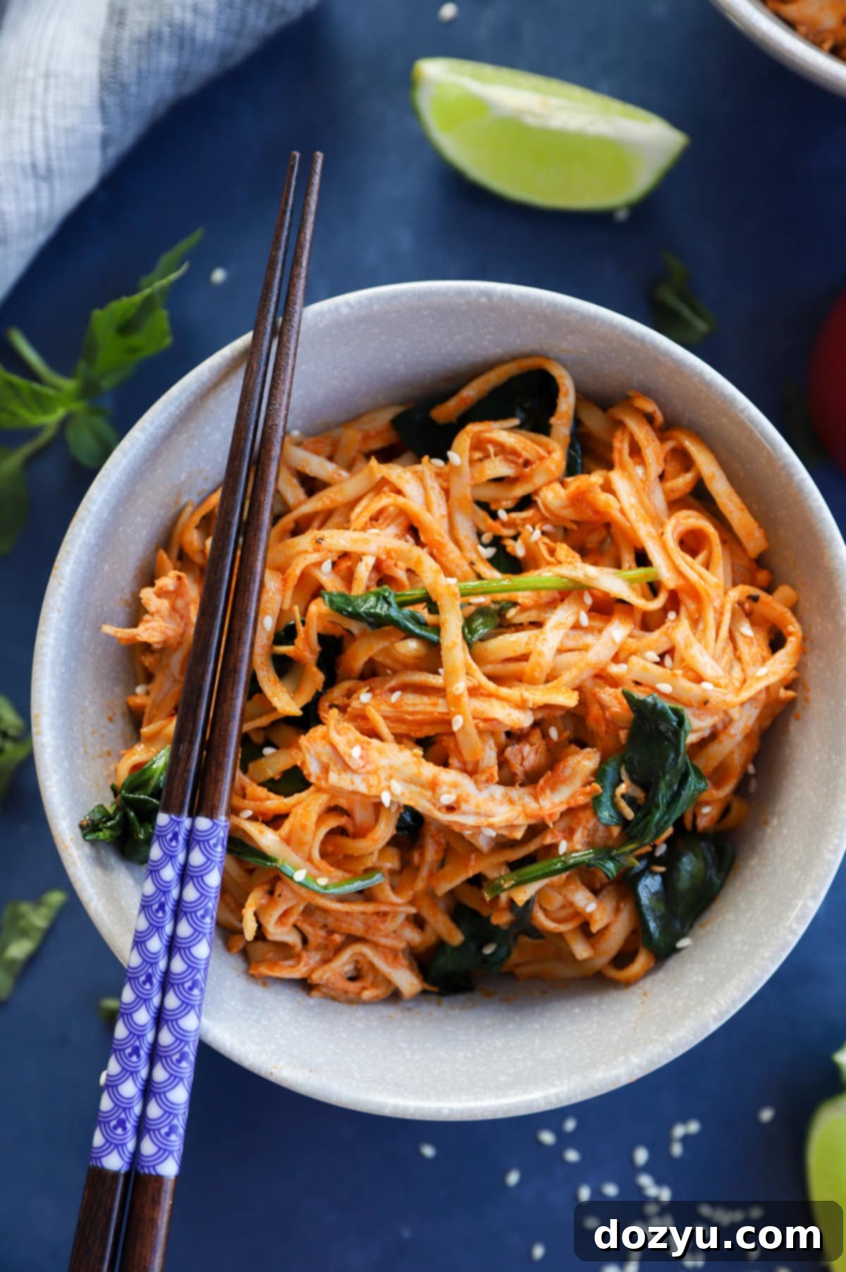 Gochujang Noodles with Chicken and Spinach in a bowl with chopsticks, garnished with basil