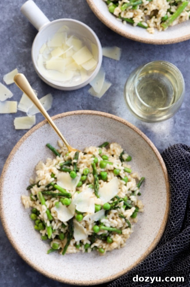 Creamy spring asparagus and pea risotto garnished with Parmesan cheese and fresh herbs, served with a glass of white wine.