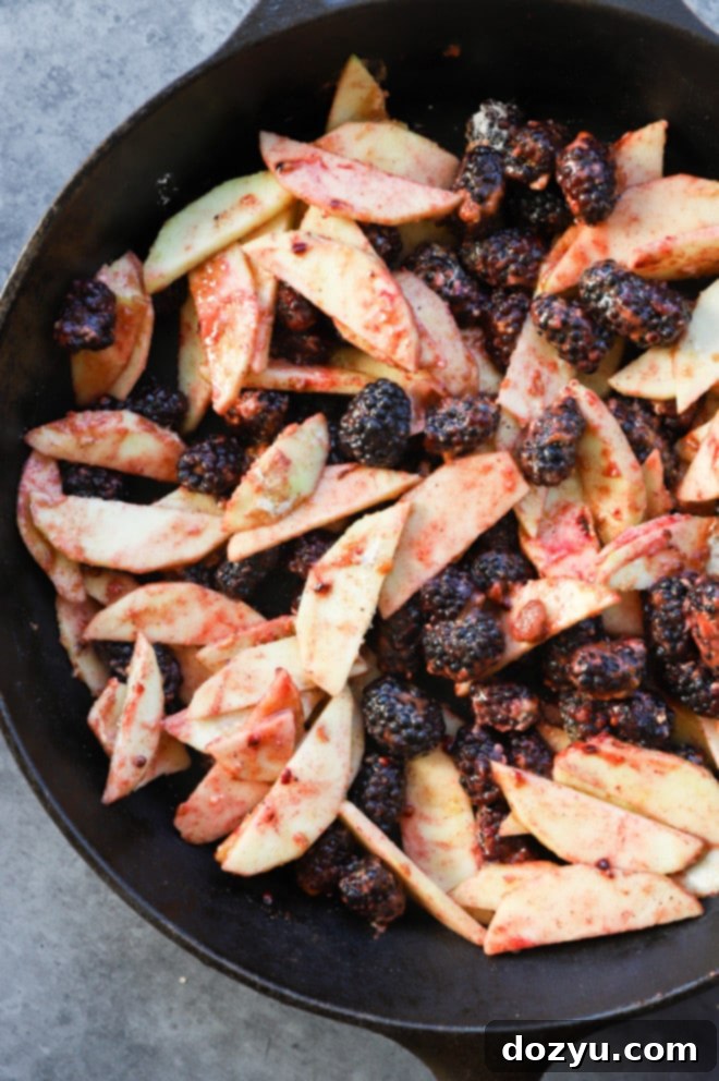 Close-up image of the vibrant fruit filling, with sliced apples and whole blackberries, ready in a cast iron skillet