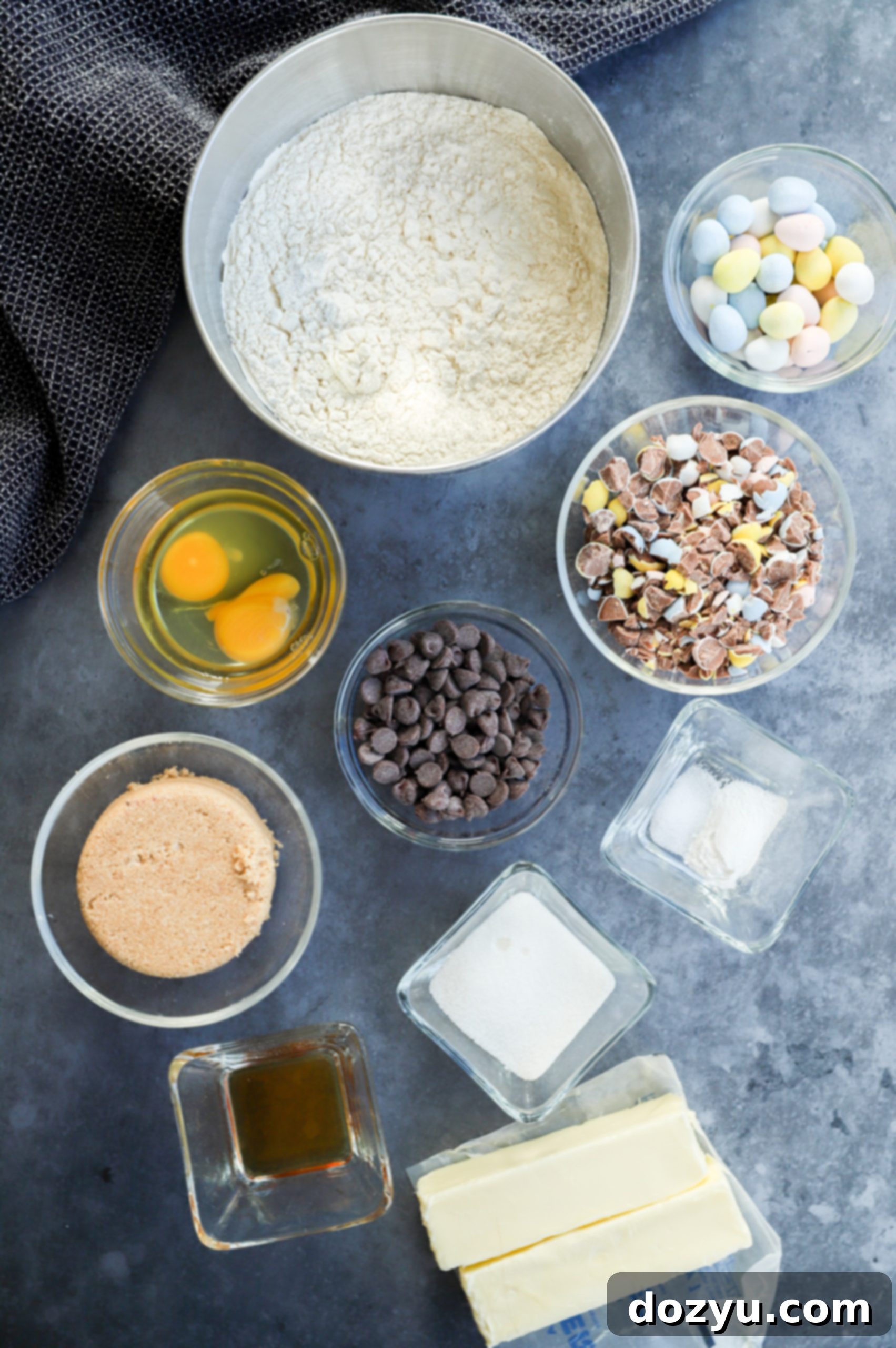 Bowls filled with the key ingredients for Mini Eggs Cookies, including flour, sugars, and the colorful Cadbury Mini Eggs.