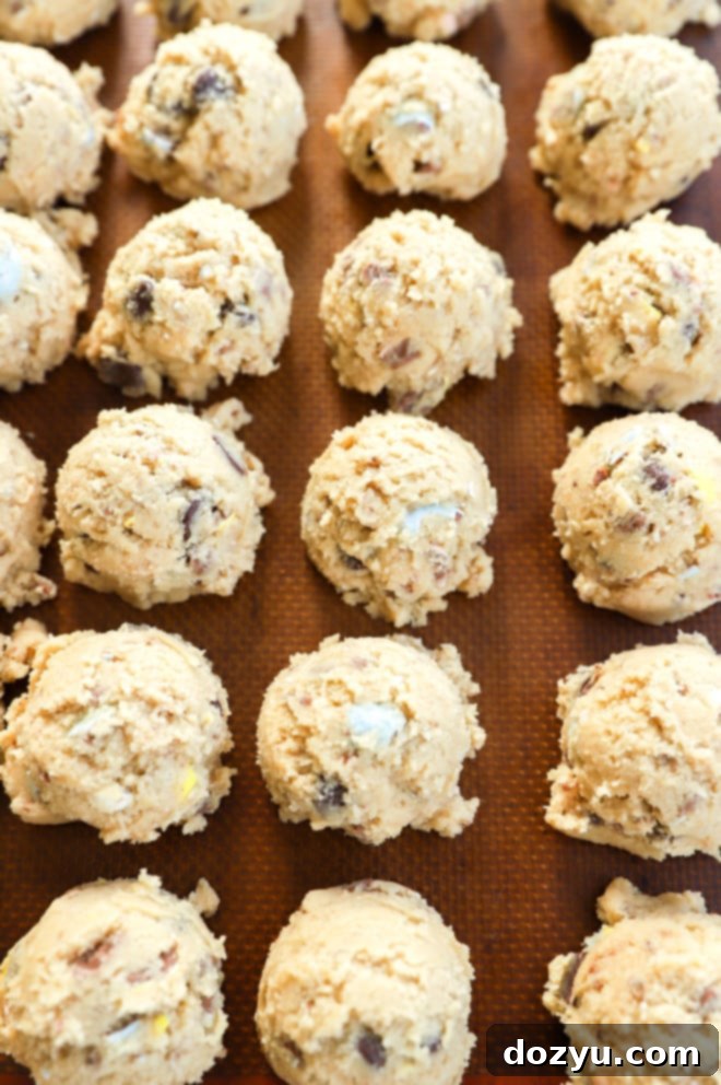Scooped cookie dough balls, studded with Cadbury Mini Eggs, neatly arranged on a baking sheet, ready for chilling.