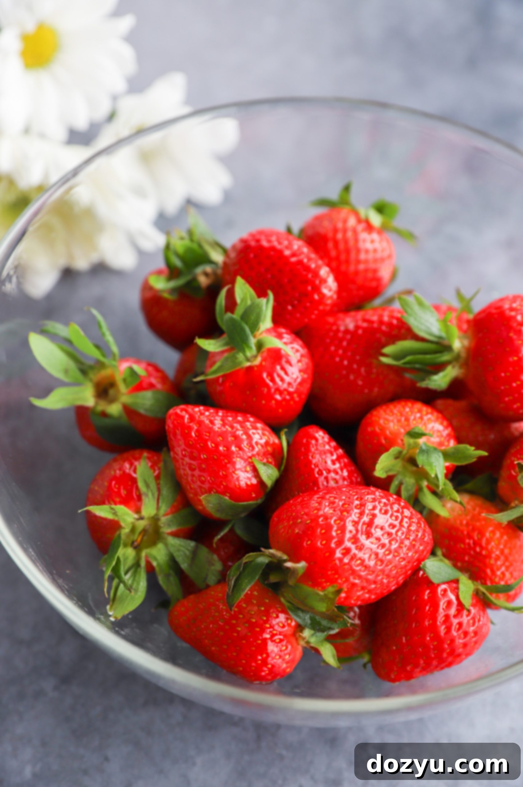 A bowl filled with fresh, ripe strawberries, surrounded by delicate flowers, highlighting the natural beauty of the fruit