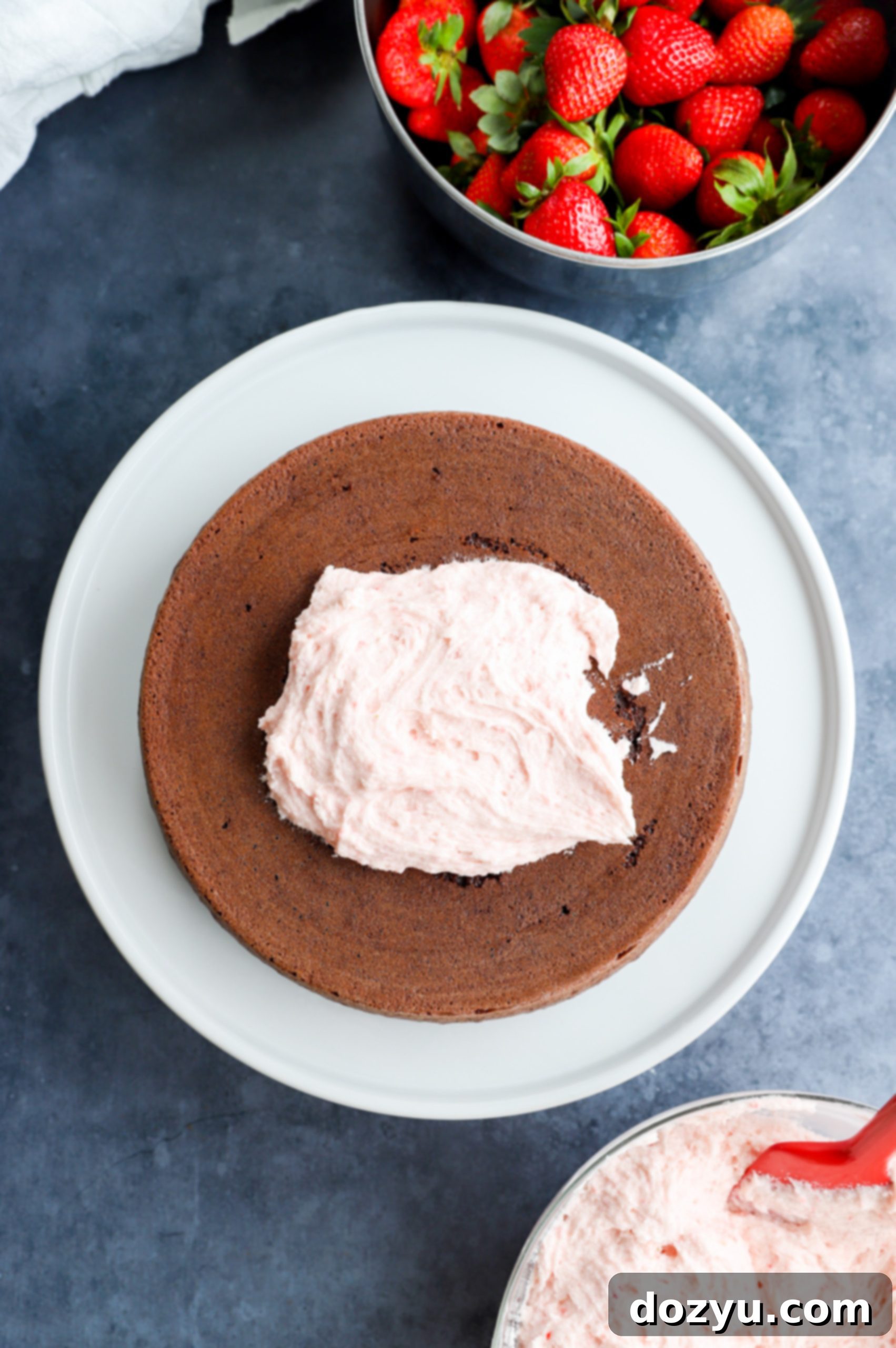 A partially frosted cake in a stand mixer bowl, ready to be decorated with fresh strawberries, demonstrating the perfect texture for application