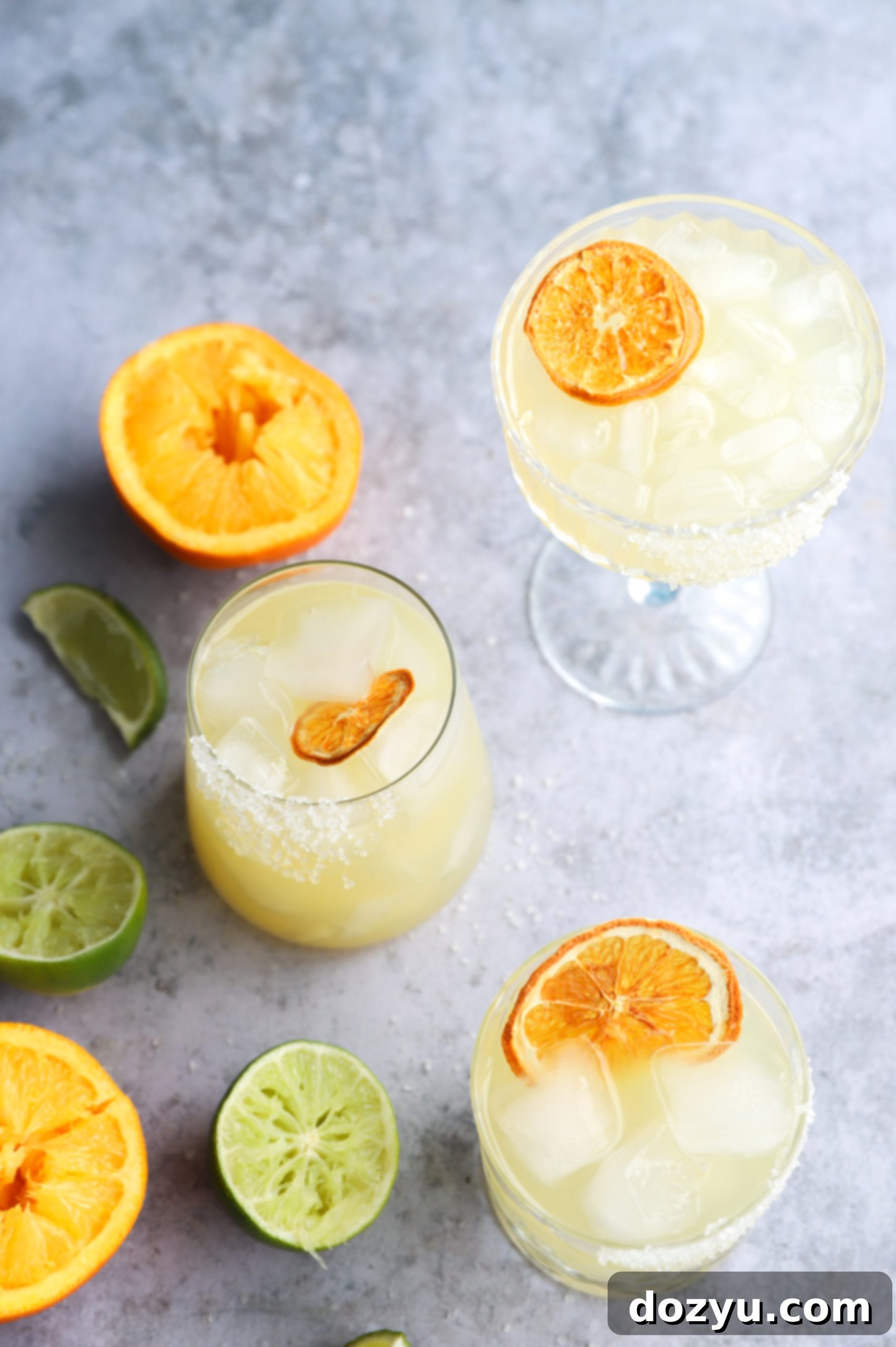 Two Texas Margaritas in glasses, garnished with fresh orange slices, sitting on a wooden surface with a pitcher of the cocktail nearby.
