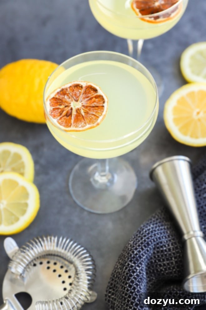 A vibrant yellow Limoncello Martini in a classic martini glass, garnished with a lemon twist, set against a blurred background.