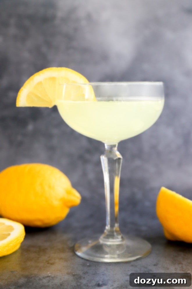 A chilled vodka lemon drop cocktail in a coupe glass, garnished with a fresh lemon slice, sits on a rustic wooden surface.