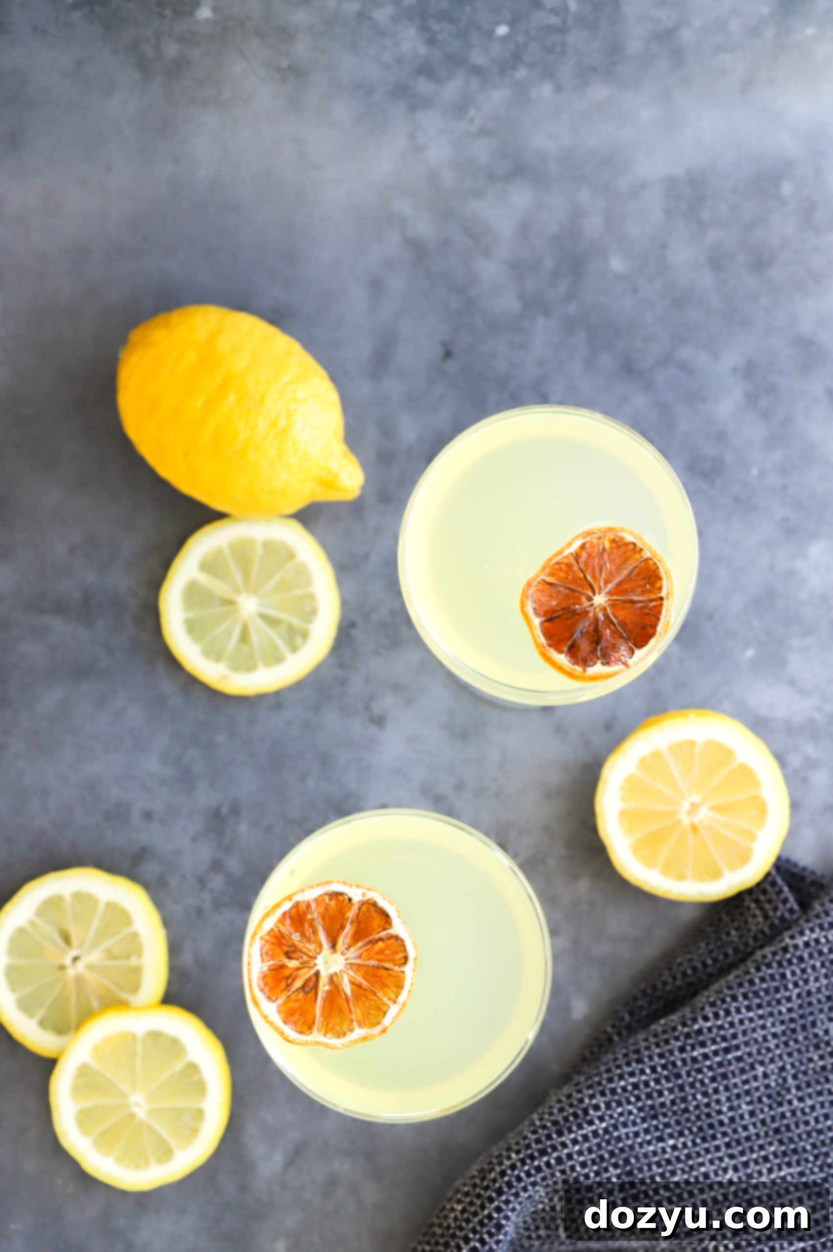An overhead shot showcasing two beautifully garnished lemon cocktails in coupe glasses, reflecting a vibrant yellow hue.