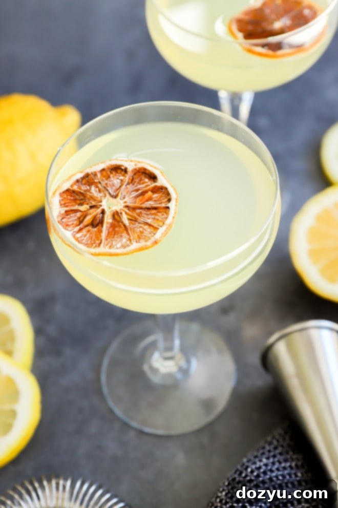 A pair of elegant lemon drop martini cocktails in glasses, with a jigger and fresh lemon slices on a wooden surface.