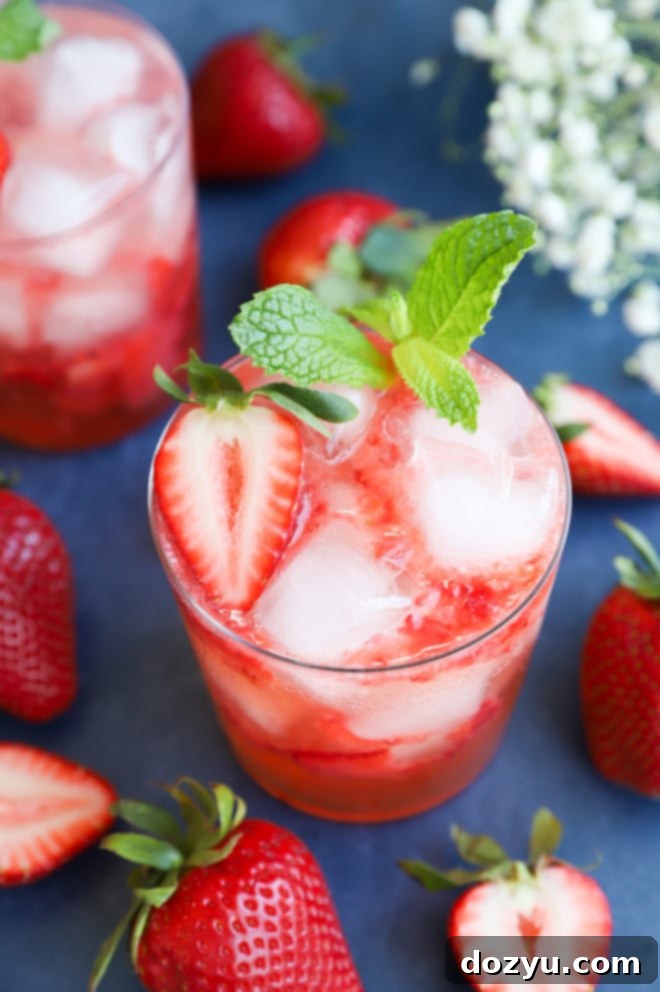 A tall glass of Strawberry Gin Smash cocktail garnished with fresh mint and strawberries