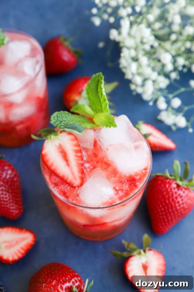 A Strawberry Gin Smash cocktail being stirred in a glass with ice and garnishes.