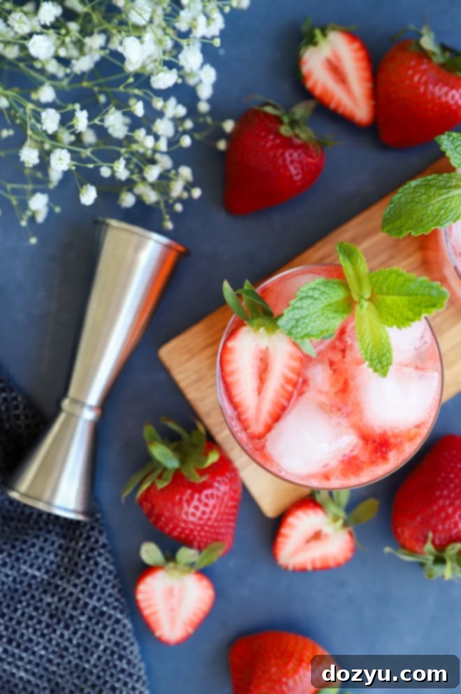 A Strawberry Gin Smash cocktail with a mint sprig, lime wedge, and strawberries on a dark background.