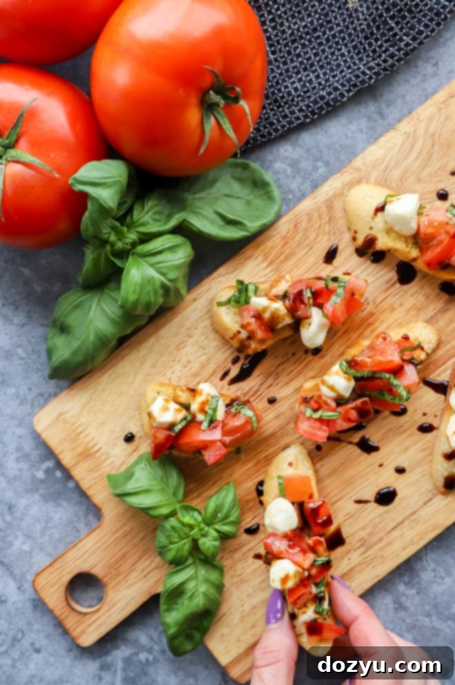 Overhead image of caprese bruschetta on platter with hand holding piece