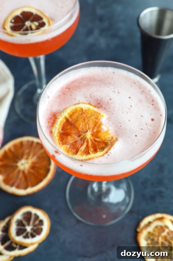 Overhead photo of an Aperol Sour cocktail with a thick foam top and orange slice garnish