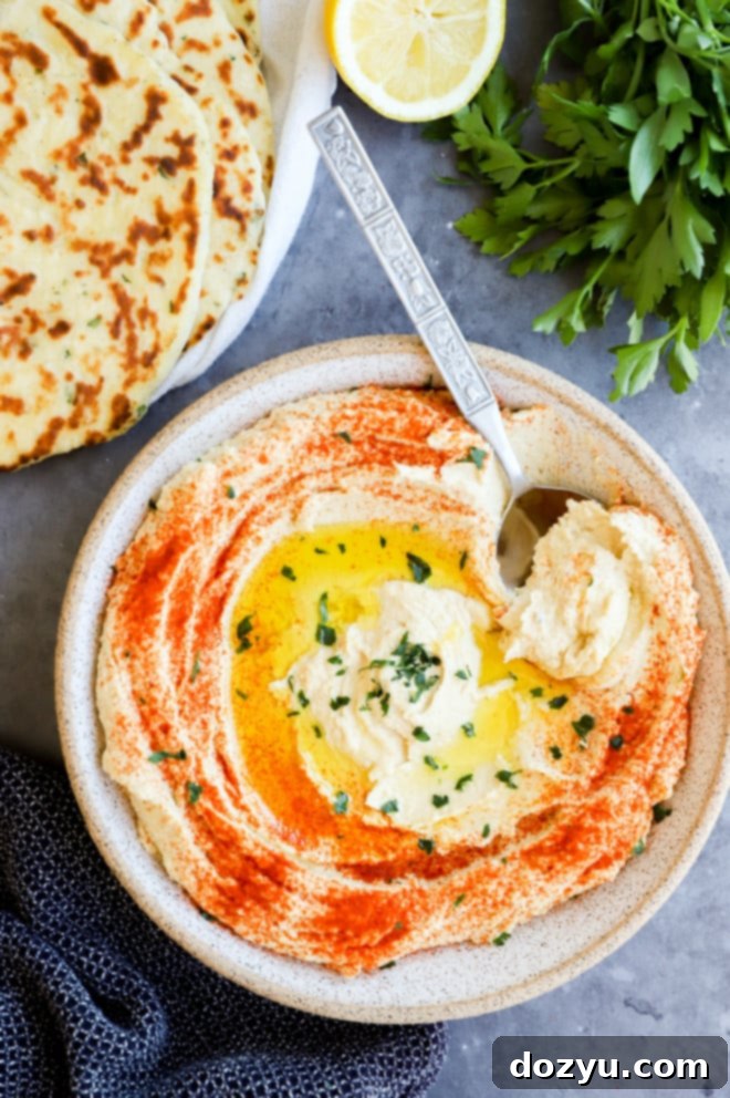 Image of creamy hummus in a bowl with a spoon, garnished with olive oil and paprika