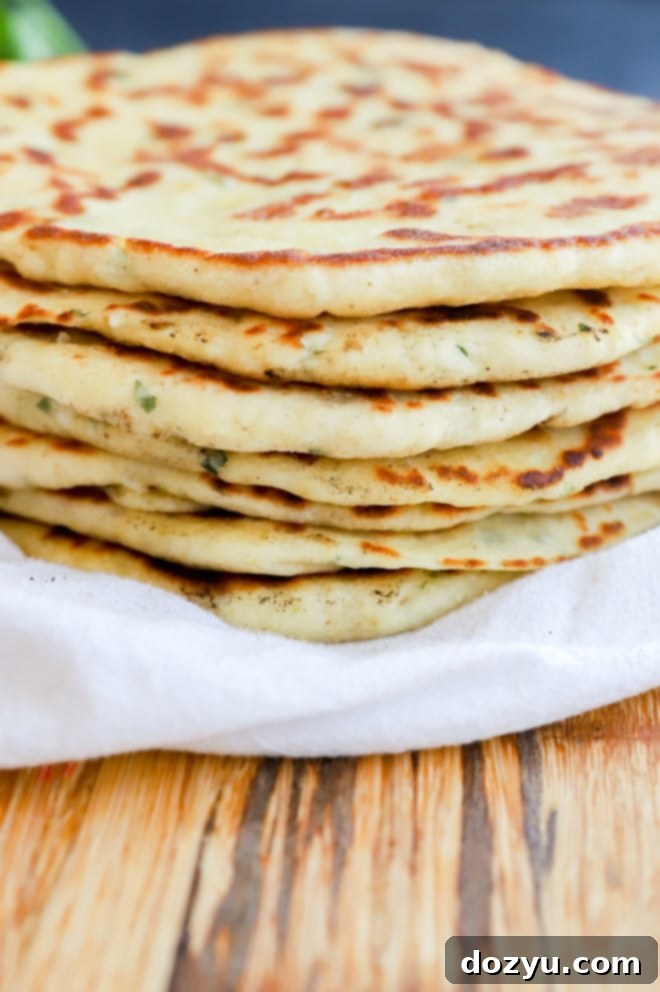 A beautifully arranged stack of herb-infused flatbreads, likely Bazlama, garnished with fresh herbs and ready to be enjoyed.