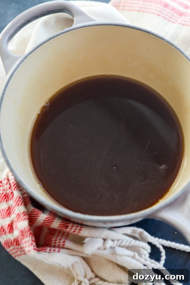 Hands stirring demerara sugar and water in a saucepan over a stovetop, illustrating the syrup-making process.