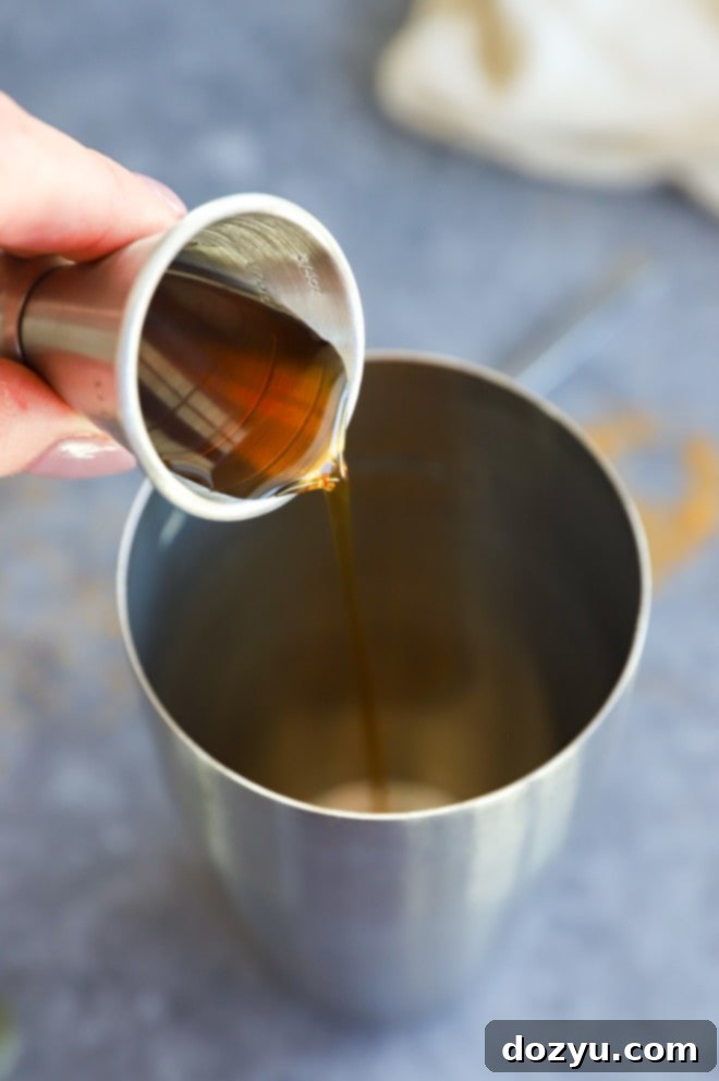 Pouring golden demerara syrup into a cocktail shaker as part of a drink preparation.