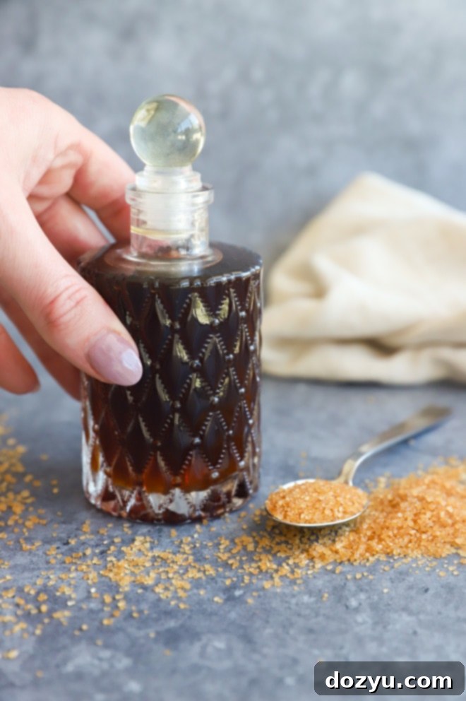 A hand holding a clear glass bottle filled with golden demerara syrup, ready for use.
