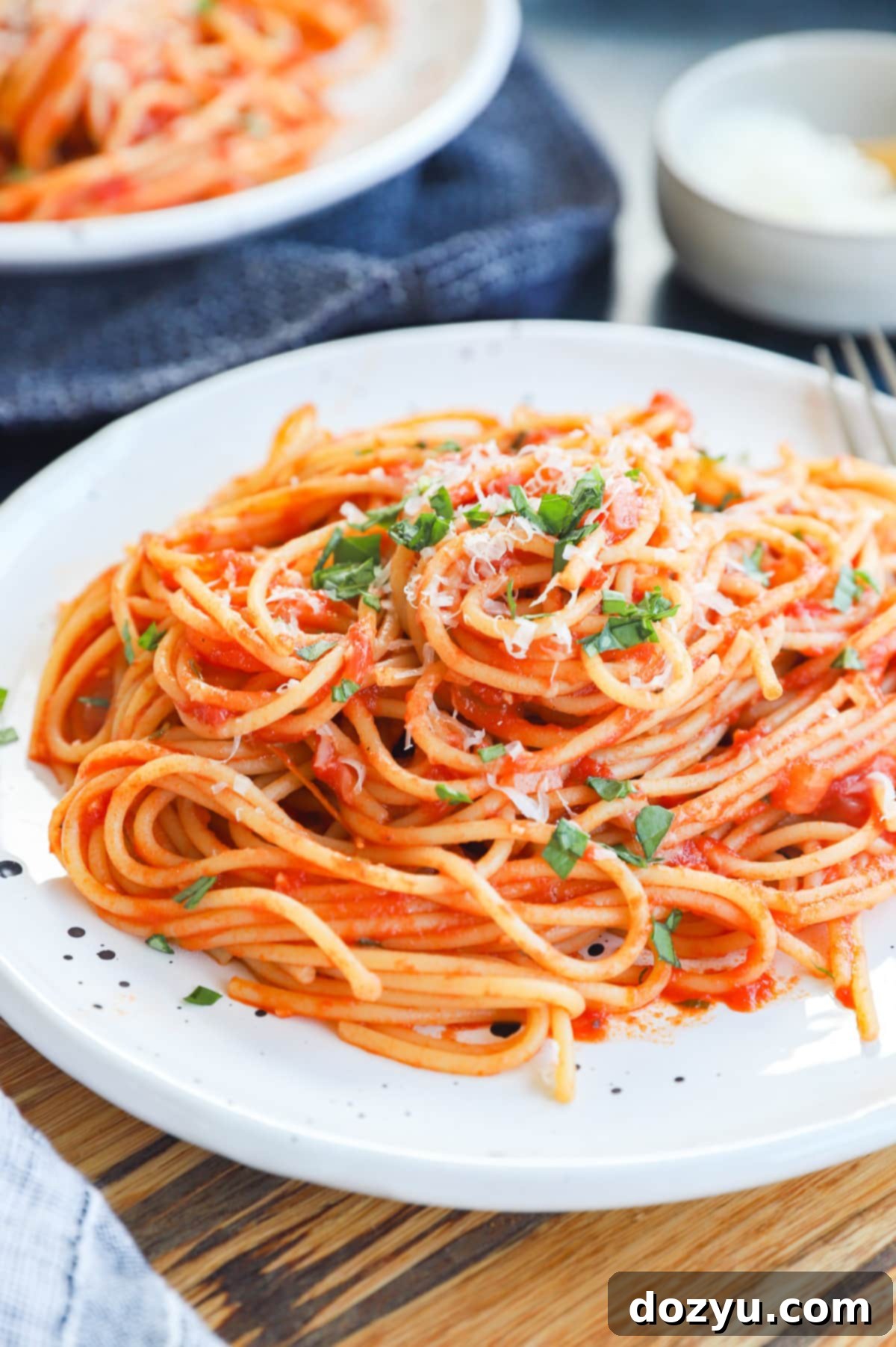 A classic plate of Pasta Napolitana, garnished generously with fresh basil leaves and freshly grated parmesan, captured in a warm, inviting light.