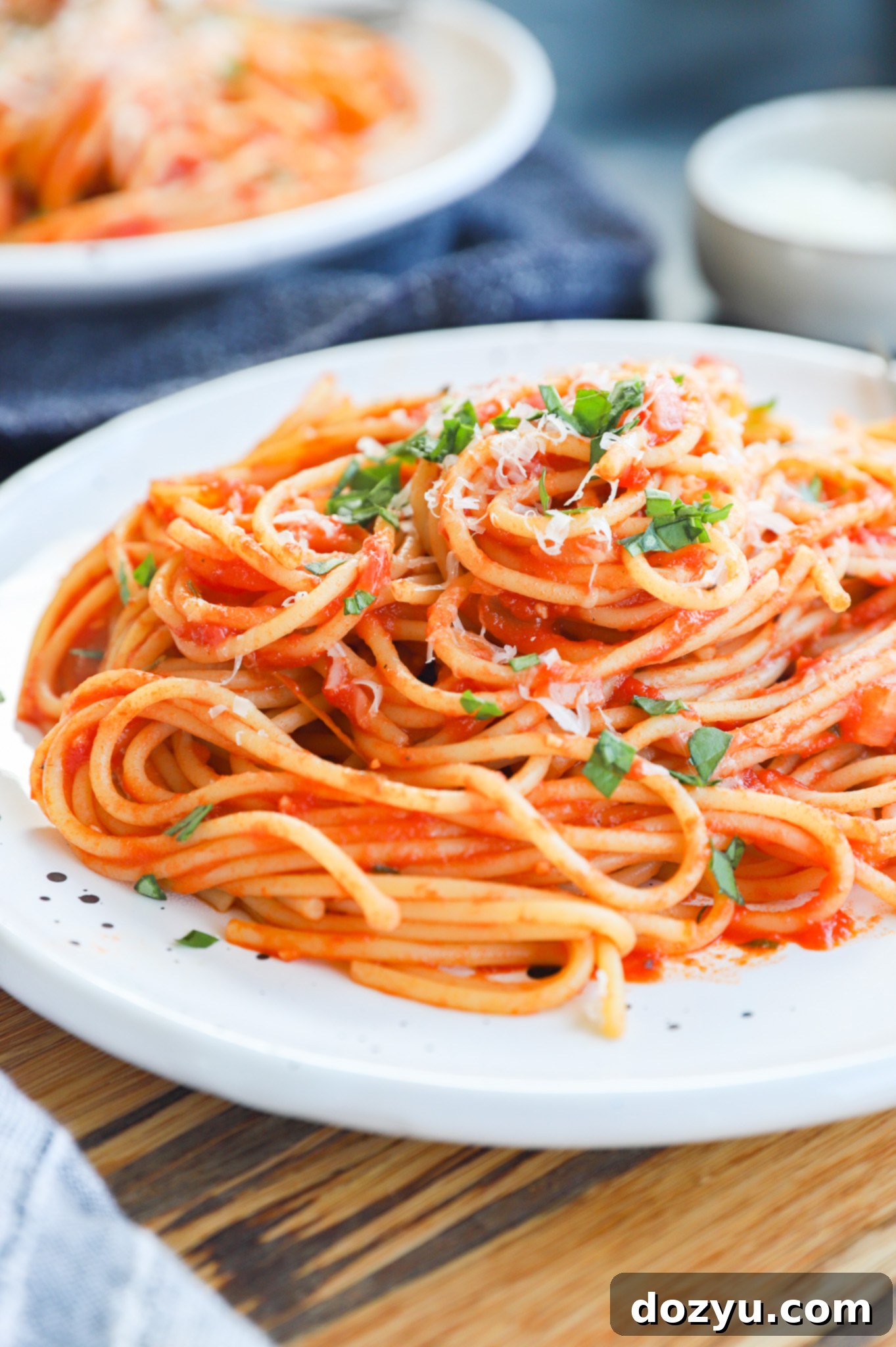 A close-up shot of a plate of Pasta Napolitana, generously topped with fresh basil leaves and freshly grated parmesan cheese.