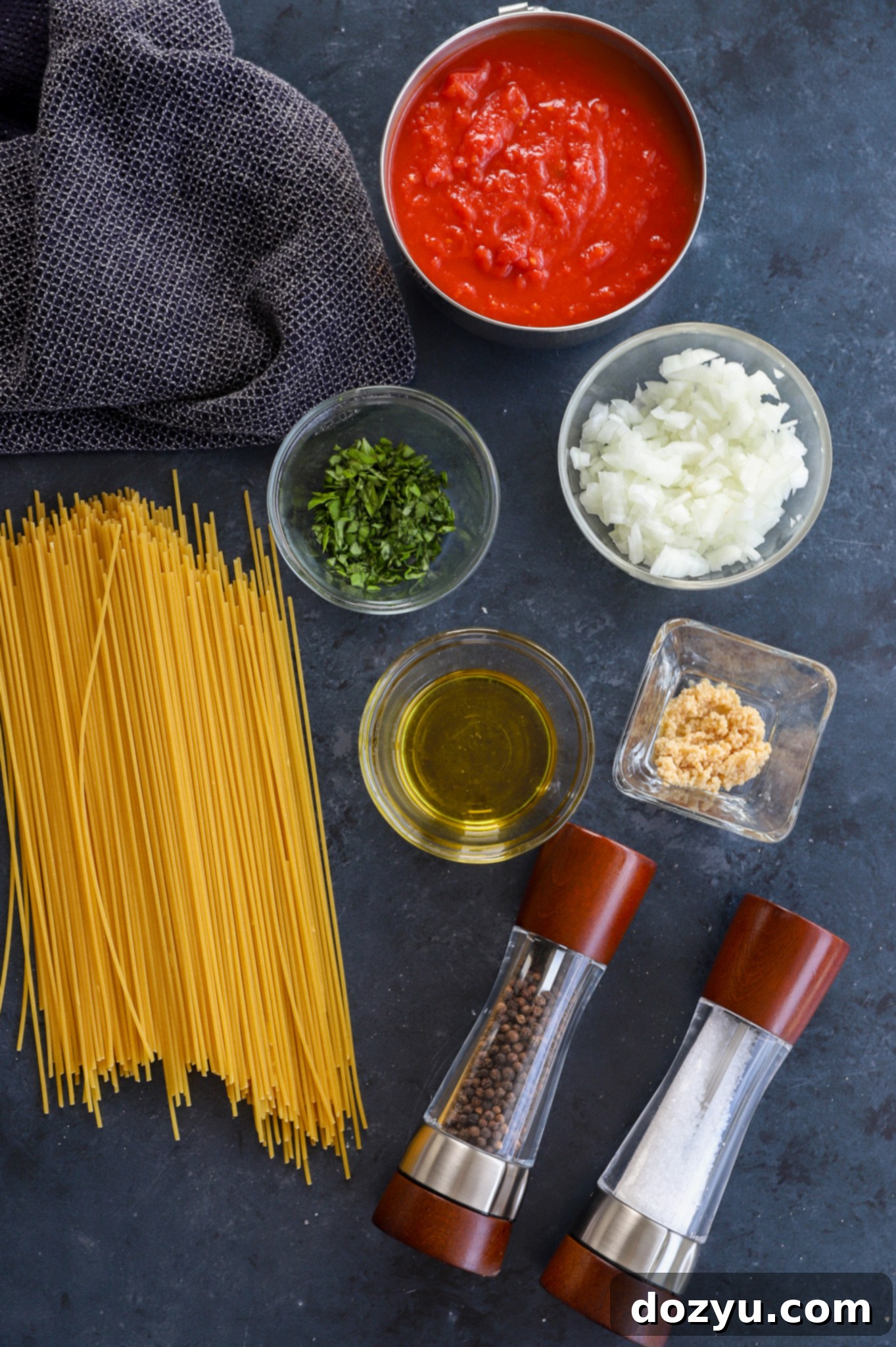 Various fresh ingredients for Pasta Napolitana laid out, including tomatoes, basil, onions, garlic, and a bottle of olive oil.