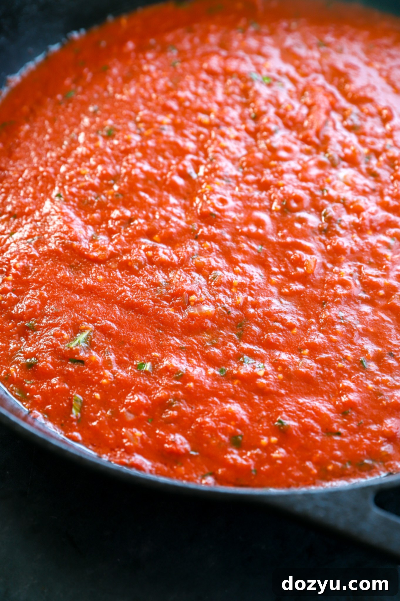 Close-up of vibrant red Italian tomato sauce simmering in a large, wide skillet, indicating rich flavor development.