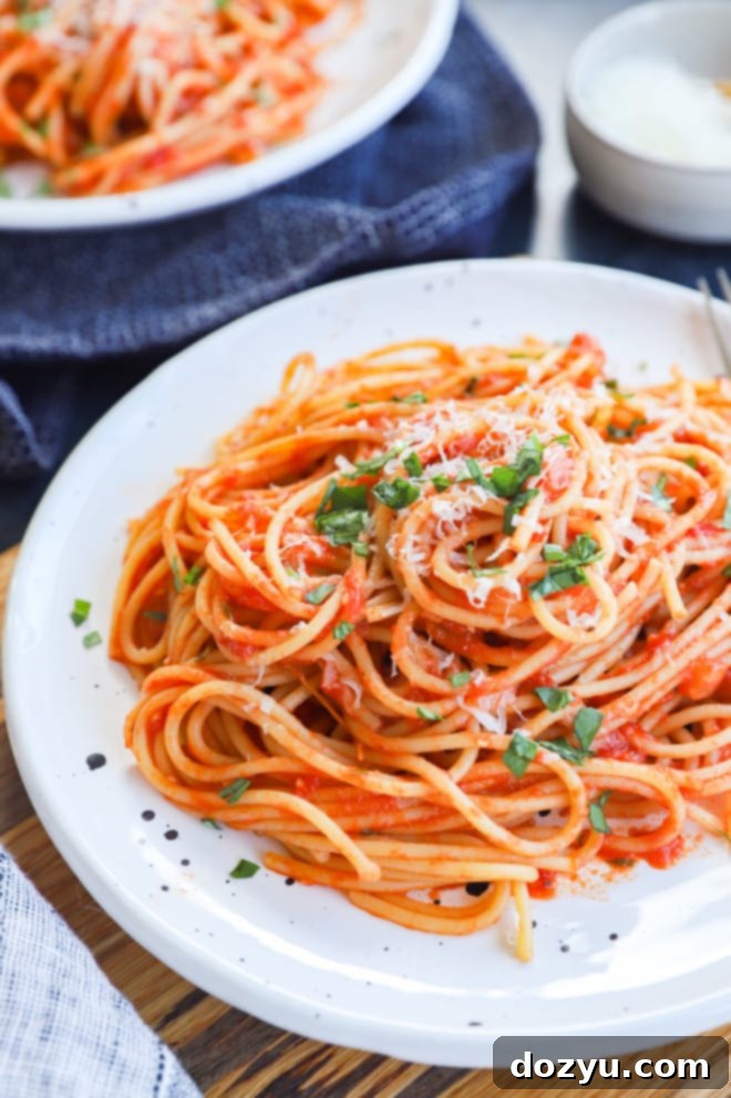 A generous serving of spaghetti with tomatoes on a plate, accompanied by a small bowl of freshly grated cheese.