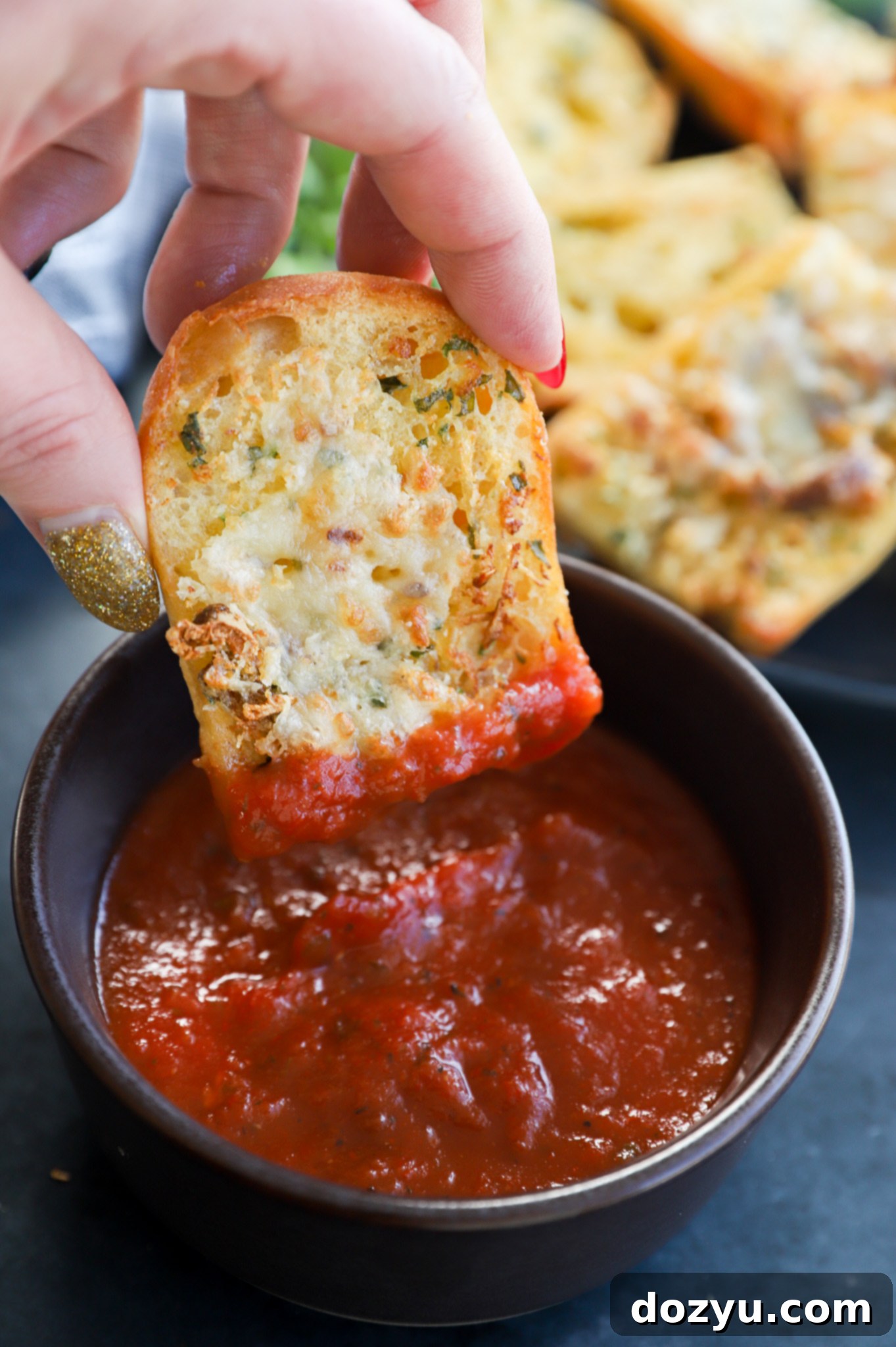A hand dipping a piece of air fryer roasted garlic bread into a sauce or oil.