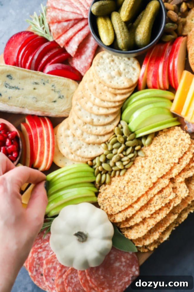 A hand reaching for a thinly sliced apple from a fall charcuterie board