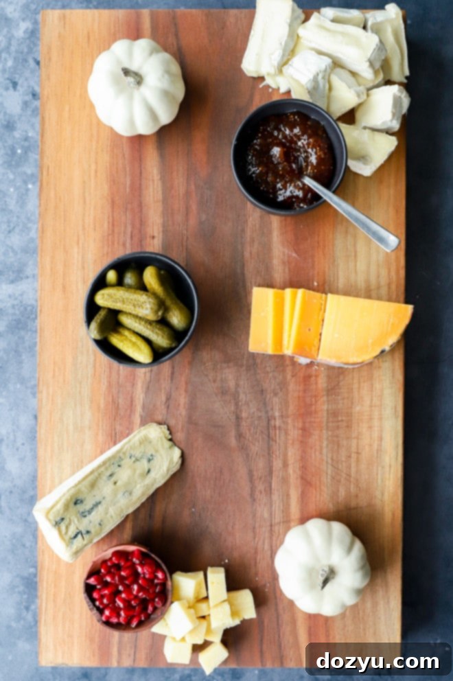 Arrangement of cheeses, dips, and honey in bowls, with decorative pumpkins, on a rustic wood board