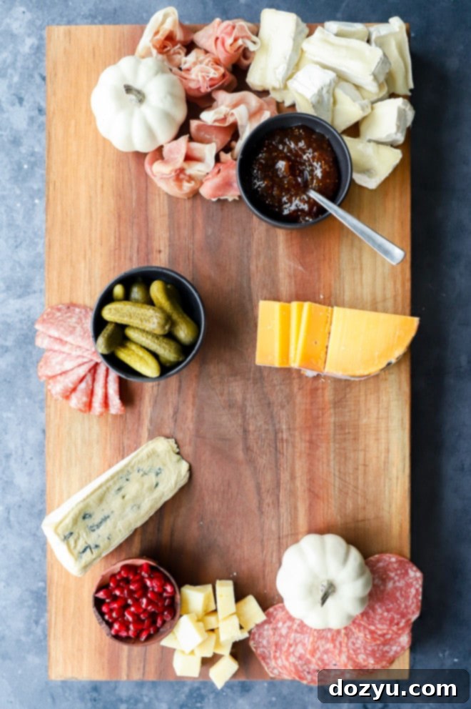 Close-up of a charcuterie board featuring cheeses, pickles, cured meats, and jam with small pumpkins for decoration