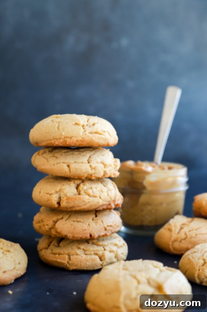 Irresistibly Chewy Peanut Butter Cookies 9 A stack of perfectly golden-brown, chewy peanut butter cookies on a white plate, with a jar of peanut butter and a scoop in the background.