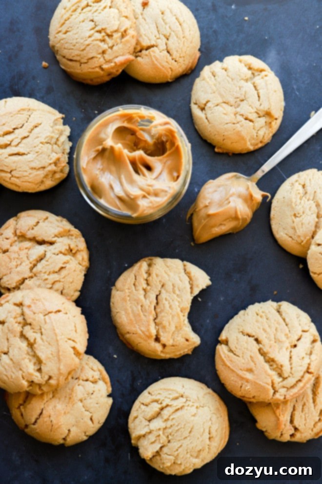 Irresistibly Chewy Peanut Butter Cookies 3 A close-up image of perfectly baked, chewy peanut butter cookies piled high on a plate, with a jar of creamy peanut butter in the background.