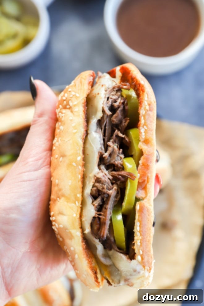 Hand holding a french dip sandwich with peppers on it