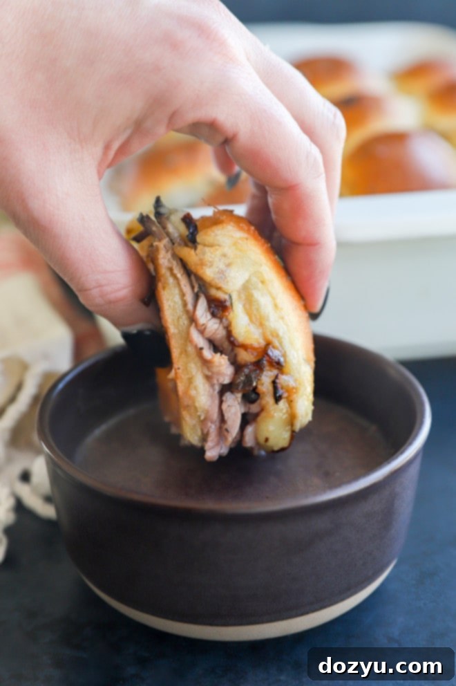 dipping a small roast beef slider sandwich in a bowl of warm au jus
