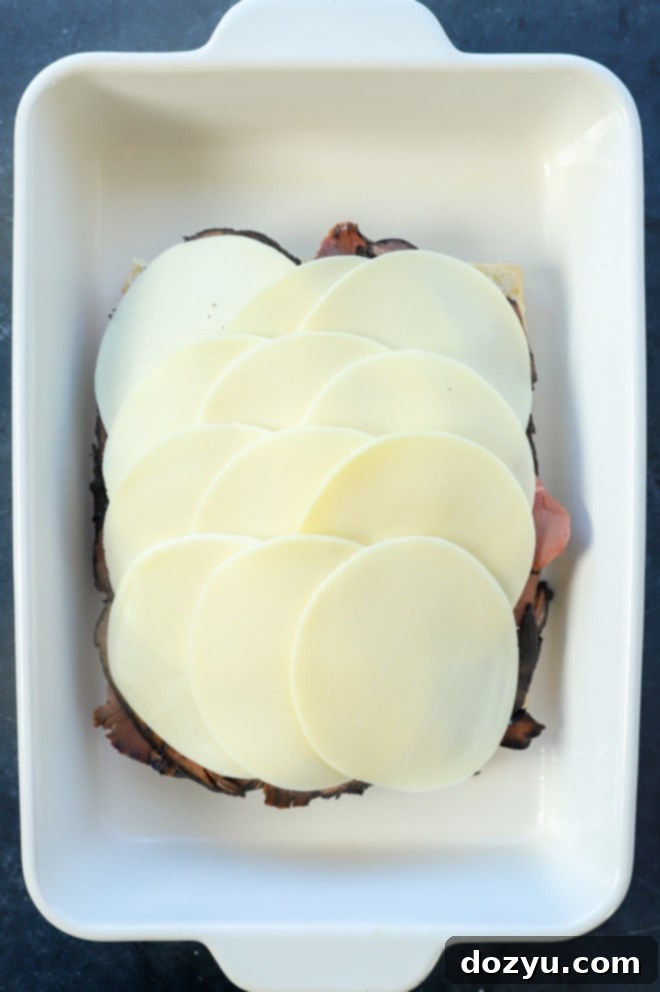 provolone cheese slices covering the roast beef layer on the rolls in a baking dish