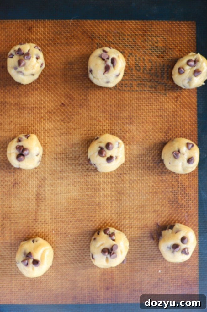Rows of tiny, perfectly formed chocolate chip cookie dough balls resting on baking sheets, awaiting their turn in the oven.