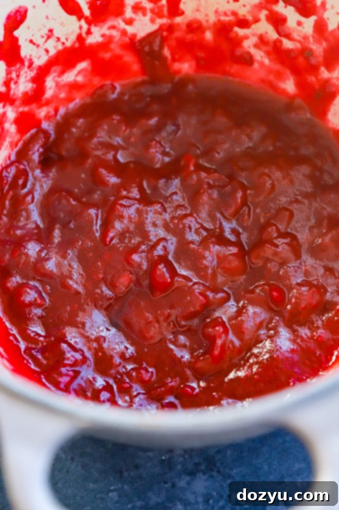 Cranberry jam simmering in a saucepan on the stove, showing bursting berries