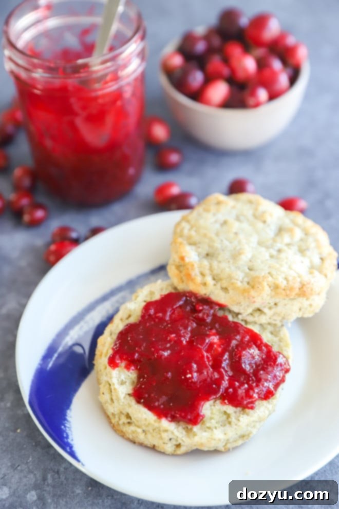 Homemade cranberry jam generously spread on a fluffy biscuit on a white plate, ready to be enjoyed