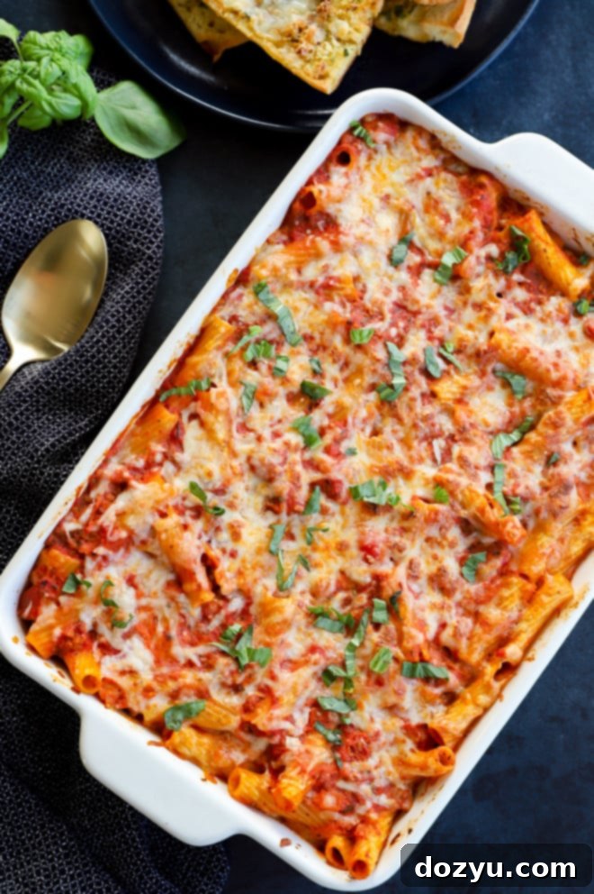 Close-up of baked rigatoni al forno with melted cheese and fresh basil in a baking dish, ready to be served.
