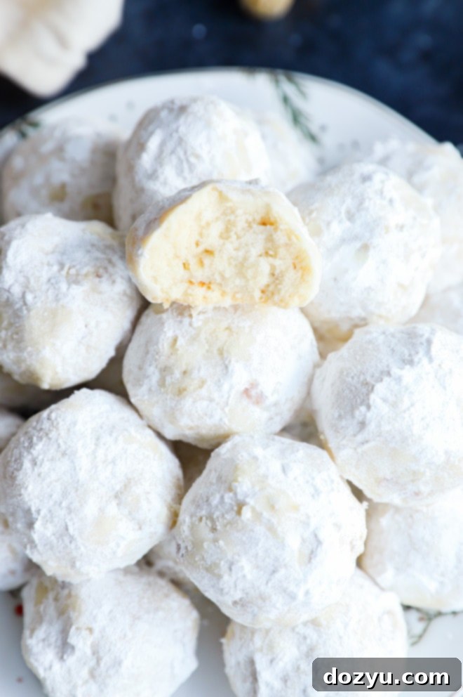 A snowball cookie with a bite taken out, resting on a pile of holiday cookies