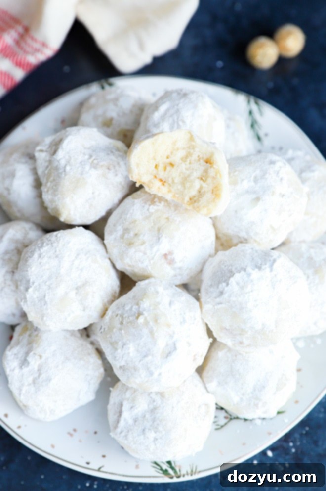 A snowball cookie with a bite taken out, resting on a pile of holiday cookies