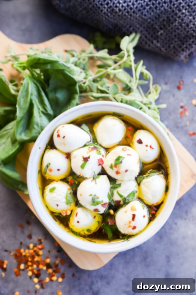 Overhead image of marinated mozzarella balls in a bowl, garnished with fresh herbs