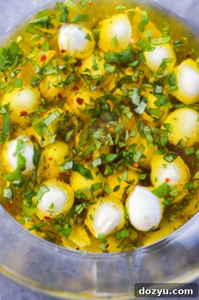 Hand stirring marinated mozzarella balls in a large glass bowl