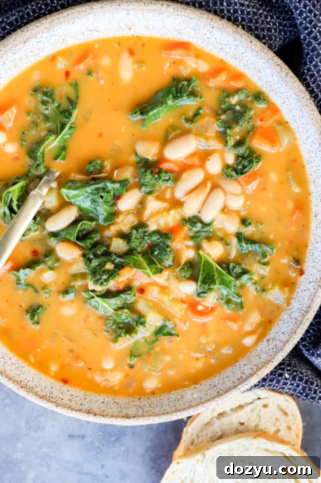 Tuscan Cannellini Bean Soup 9 Overhead image of a bowl of Tuscan white bean soup with a spoon, fresh herbs, and crusty bread